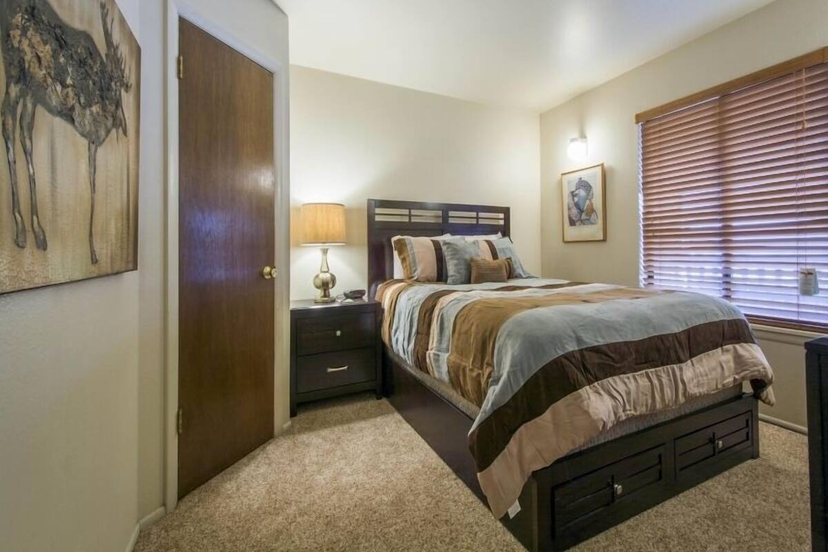 A bedroom with a bed, nightstand, lamp, and artwork on the wall.