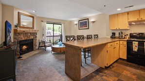 A modern kitchen with a stone fireplace, wooden cabinets, and a large island.