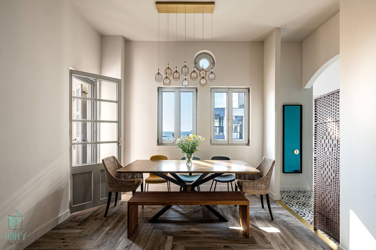 A dining area with a wooden table, wicker chairs, a bench, and hanging light fixtures.