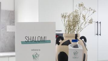 Welkomstkaart voor een hotel genaamd 'SHALOMI' met een logo, een waterfles en een vaas met bloemen op een aanrecht.