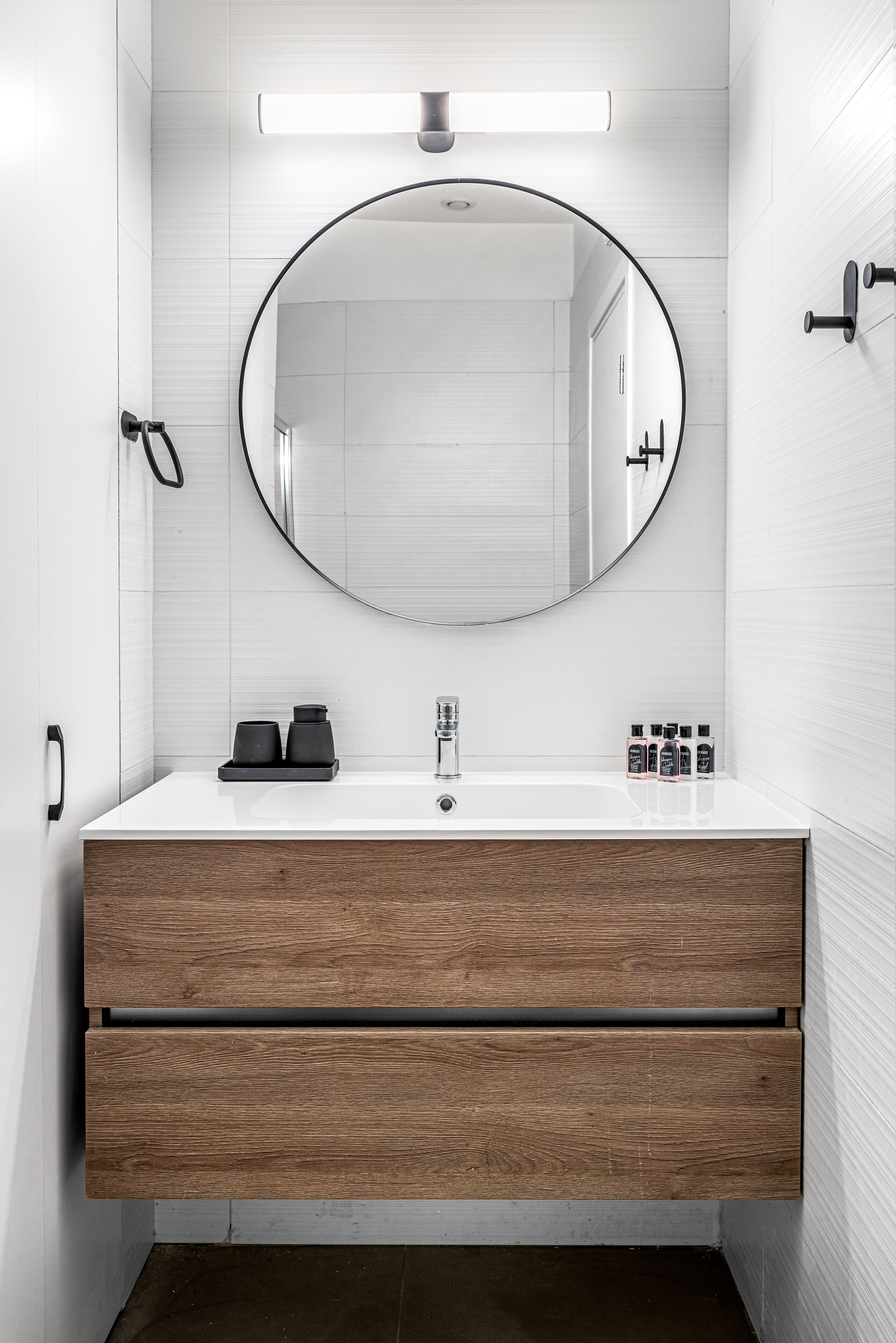 A modern bathroom with a round mirror, a white sink, and wooden drawers.