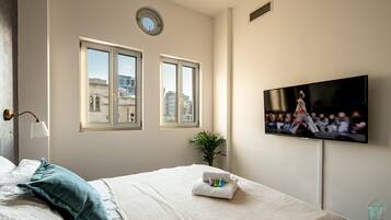 Una habitación de hotel con cama, televisor montado en la pared y ventana con vista a edificios.