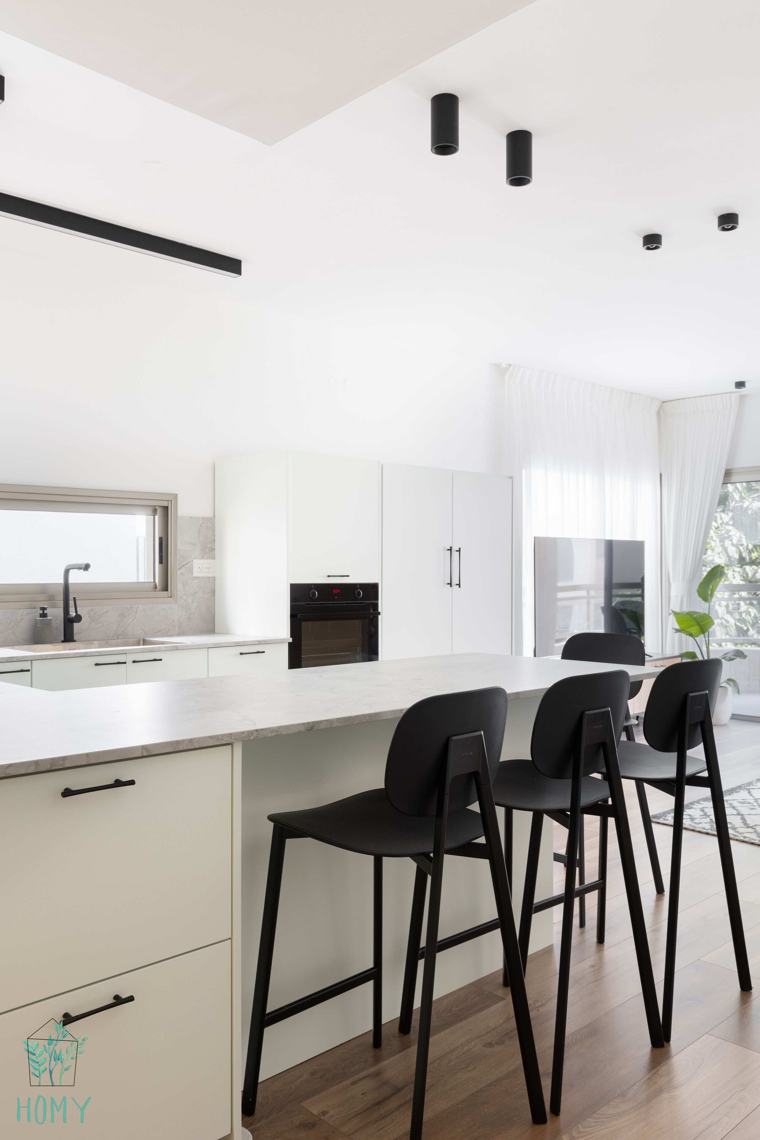 A modern kitchen with white cabinetry, a central island with bar stools, and a large window providing natural light.