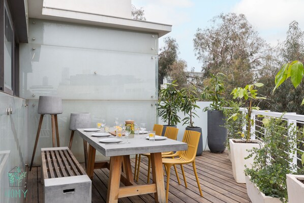 Un espace de restauration en plein air avec une table dressée pour quatre personnes, entourée de chaises jaunes, sur une terrasse en bois.