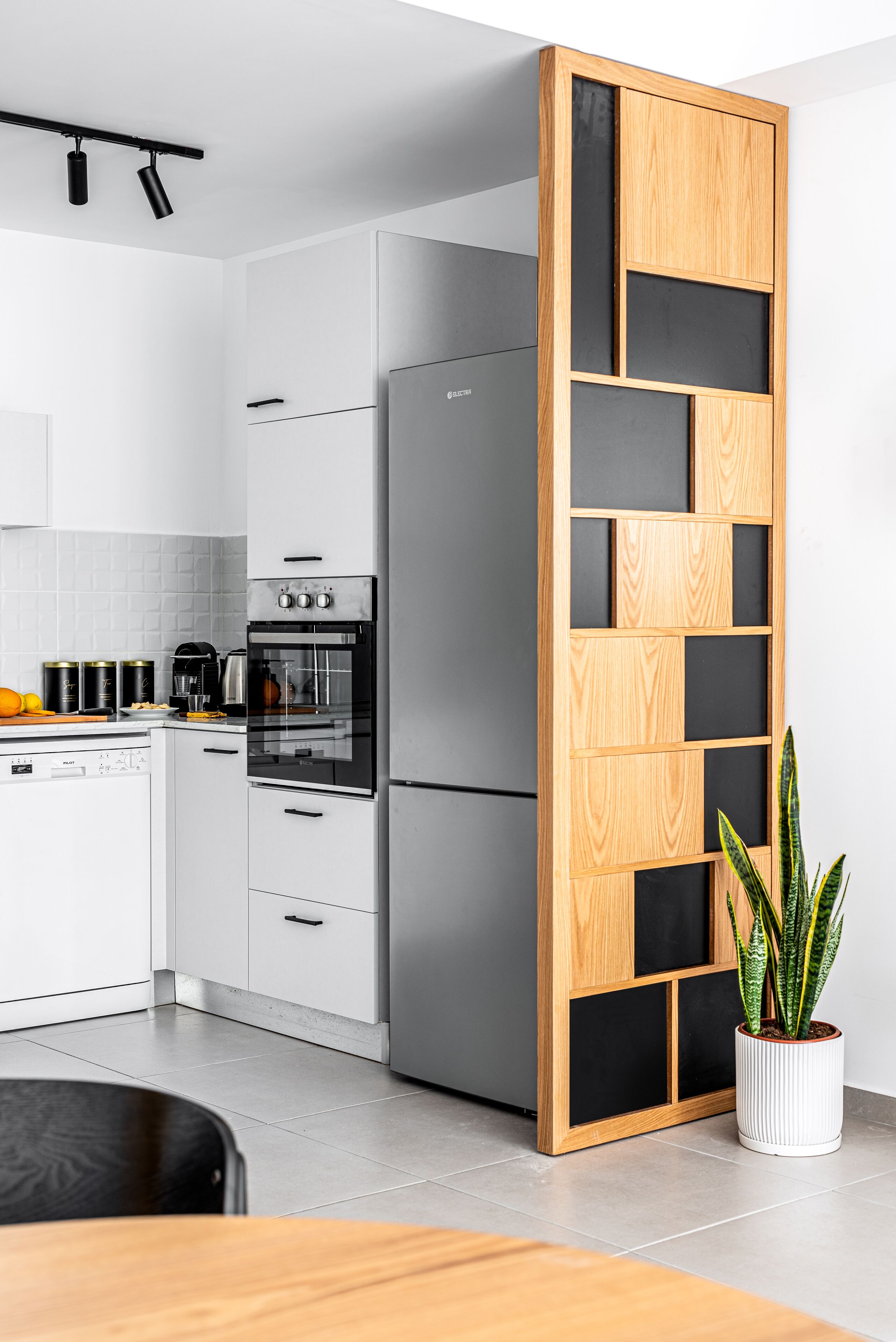 A modern kitchen with white cabinetry, a built-in oven, and a wooden partition with black panels.