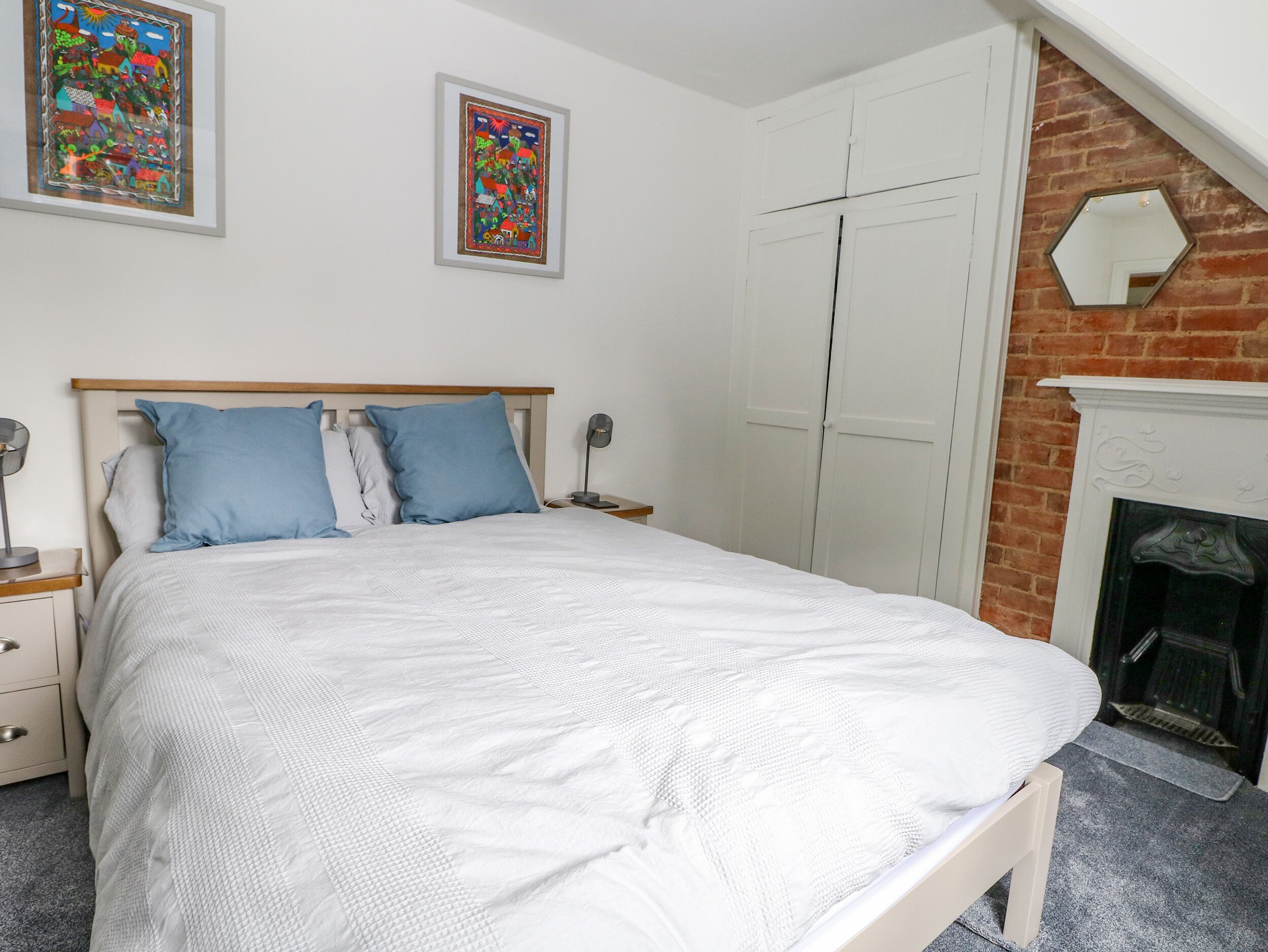A bedroom with a bed, two nightstands, a white wardrobe, a brick wall, and a fireplace.