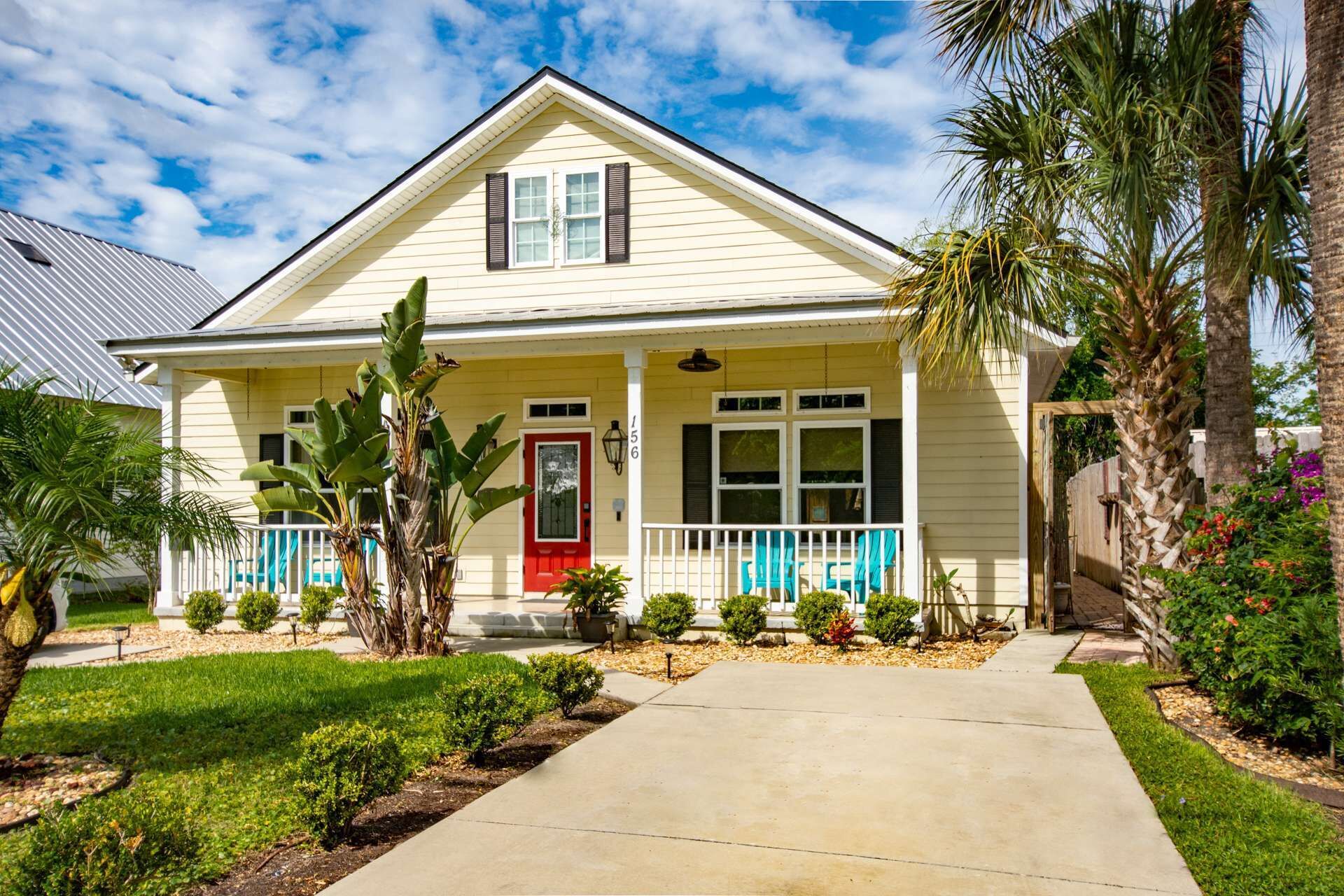 A single-story house with a red door, a front porch with blue railings, and a number '156' on the wall.