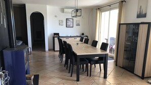 A dining area with a large table and chairs, a wood stove, and a kitchen area in the background. - Magnificent villa Chloéline: Swimming pool and superb view (Pougnadoresse)