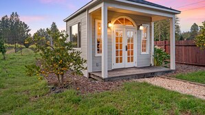 A small, single-story house with a porch, a small garden, and a wooden fence in the background.
