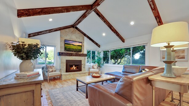 A spacious living room with a fireplace, leather sofa, and a large window offering a view of trees.