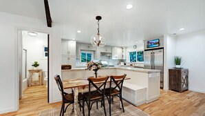 A modern kitchen with white cabinetry, a wooden dining table with four chairs, a central island, and a built-in oven.