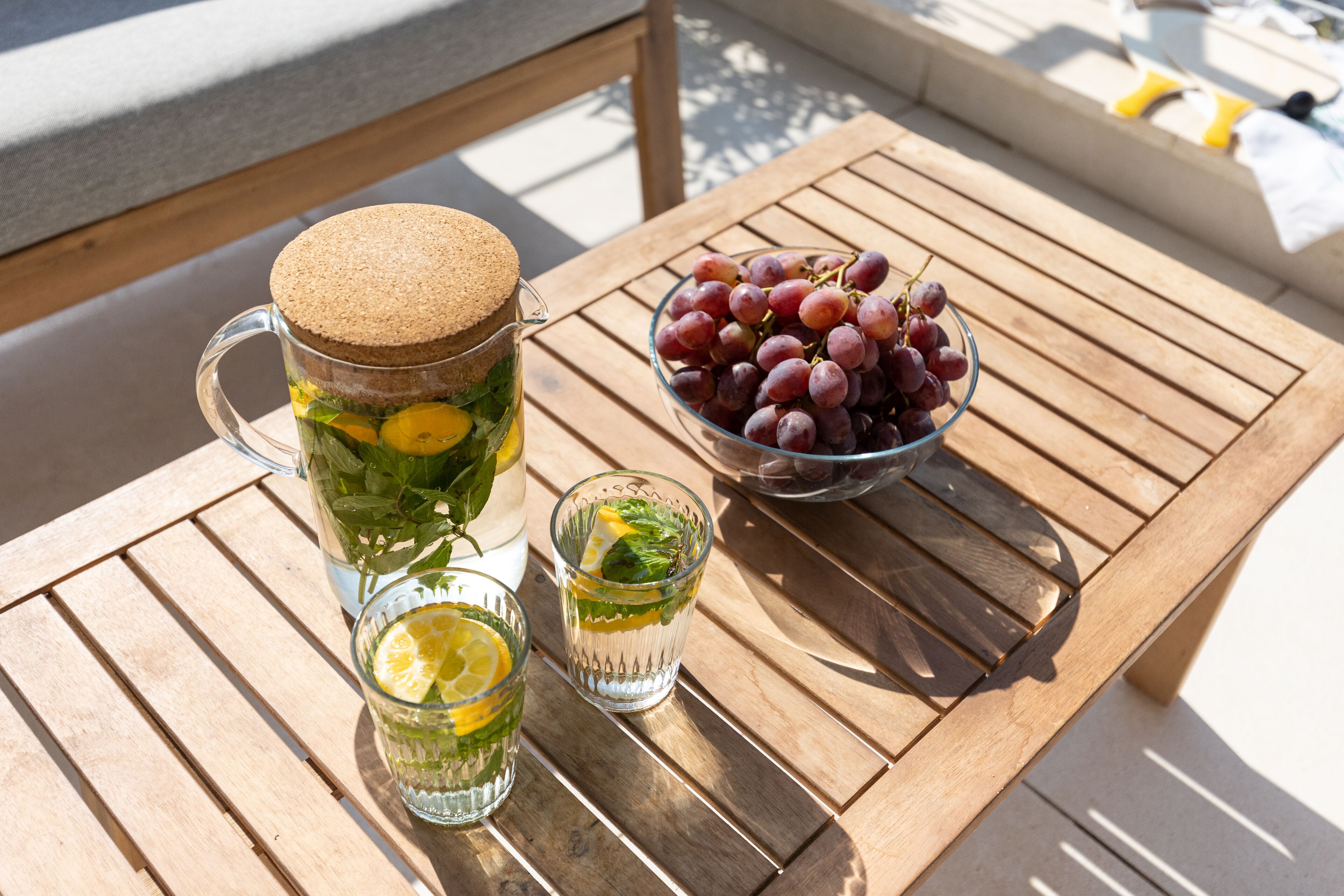A wooden table with a pitcher, a bowl of grapes, and two glasses of a lemon-lime beverage.
