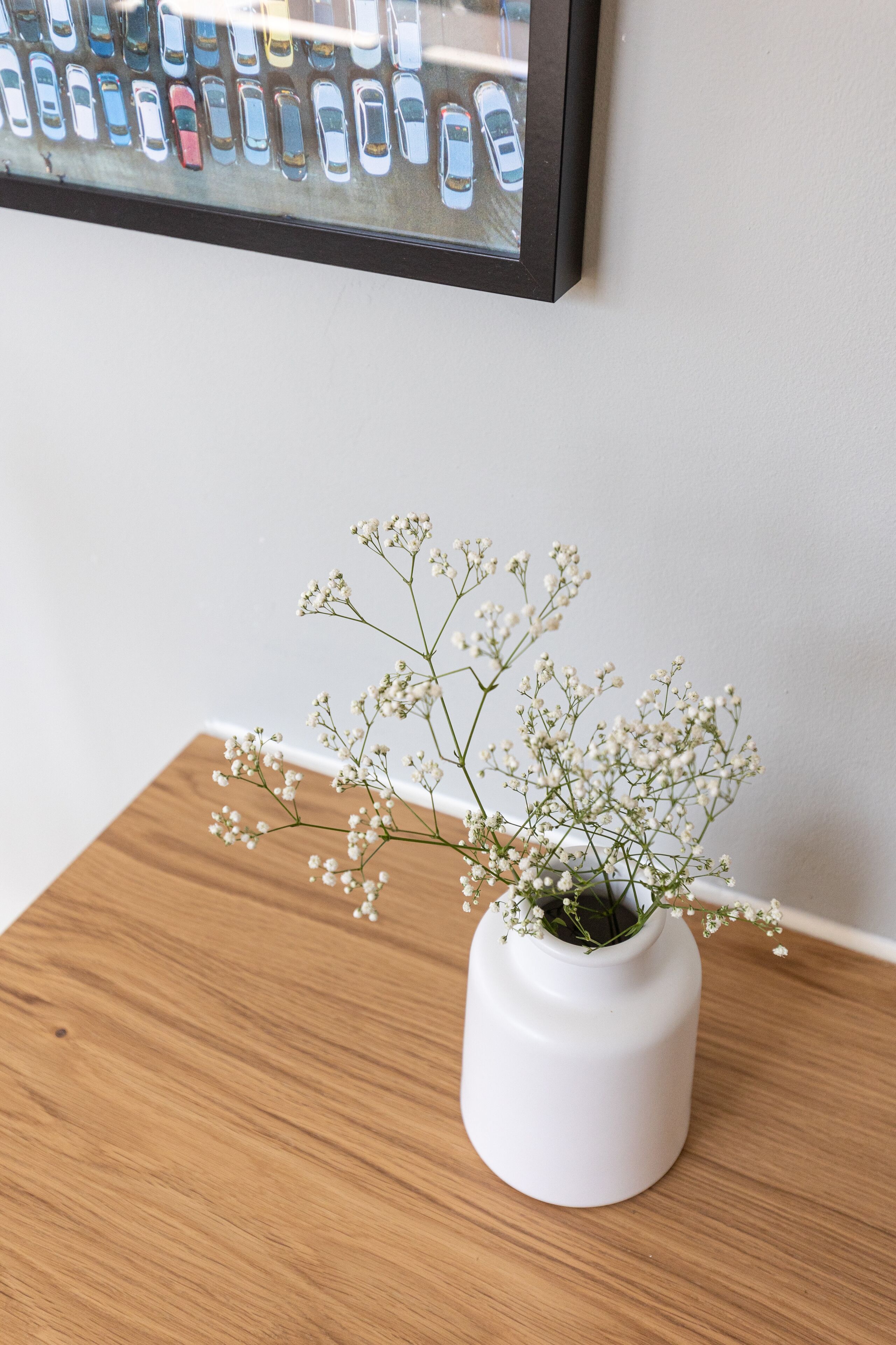 Un vase blanc orné de petites fleurs de gypsophile, posé sur une table en bois.