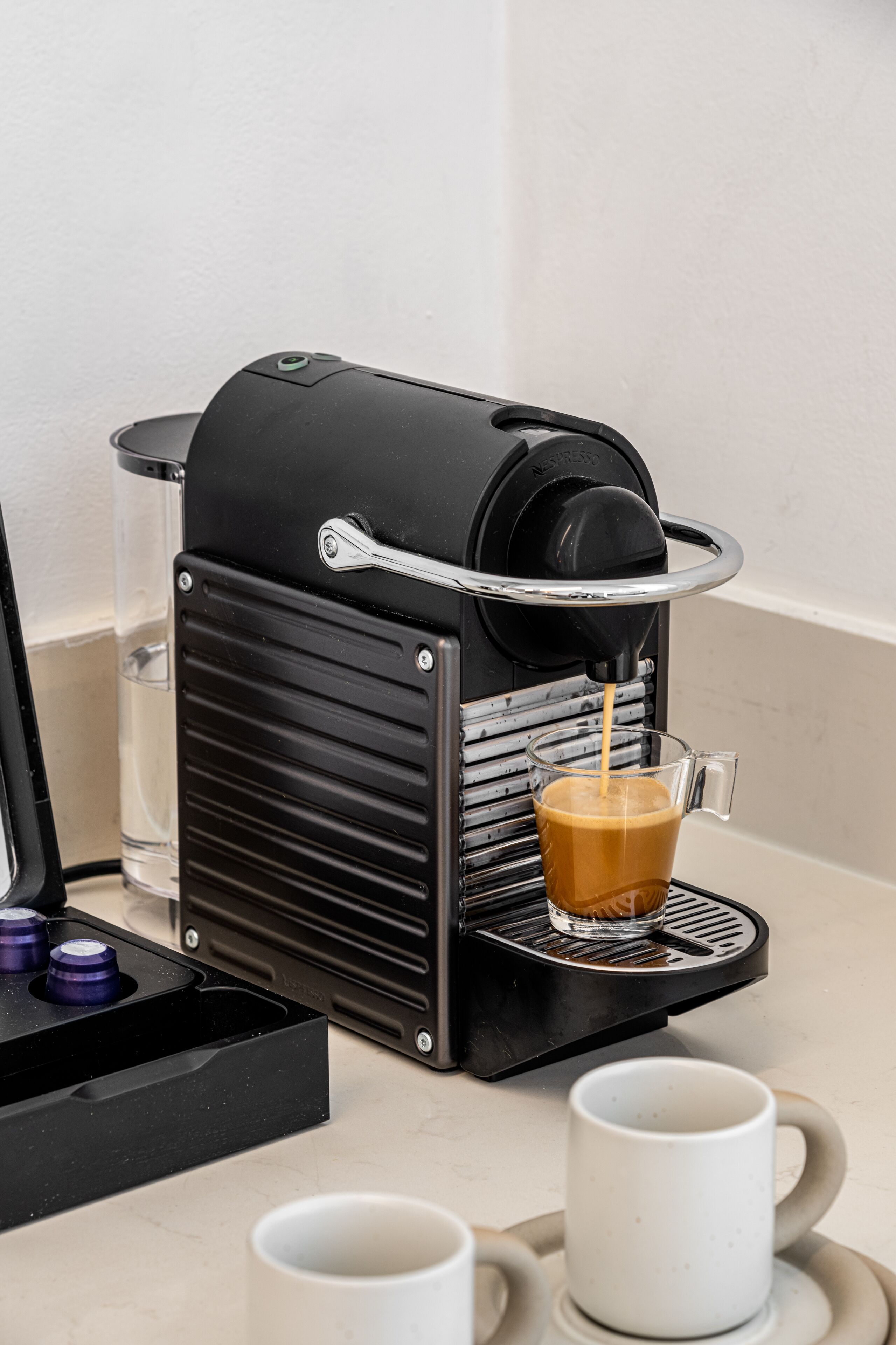 Una cafetera con una taza de vidrio en su bandeja de goteo, un depósito de agua y un preparador de café con asa.
