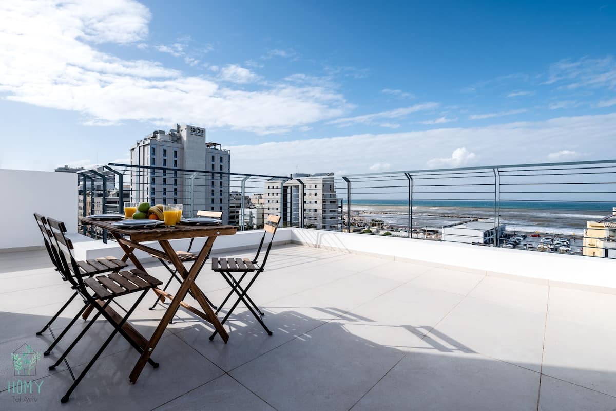 Terraza en la azotea con una mesa y sillas, vista al mar y edificios al fondo.