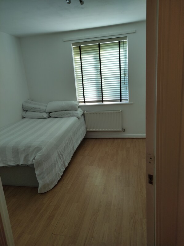 A bedroom with a bed, a radiator, and a window with blinds.