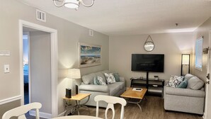 A living room with a sofa, a TV, a chandelier, and a dining table with chairs. - Resort Daze-2 Bedroom, Short Walk to the Beach (Hilton Head Island)