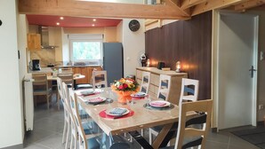 A modern kitchen with wooden cabinets, a dining area with a long table set for six, and a large window providing natural light. - Lou Vachou - Rimeize (RIMEIZE)