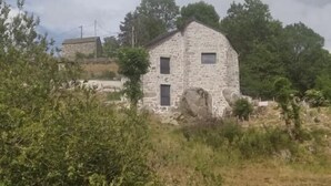A stone building with two visible windows and a door, surrounded by dense greenery and a cloudy sky. - Lou Vachou - Rimeize (RIMEIZE)