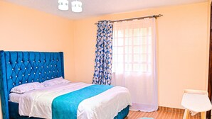 Una camera da letto con un letto imbottito blu, un comodino bianco e una tenda a fantasia.