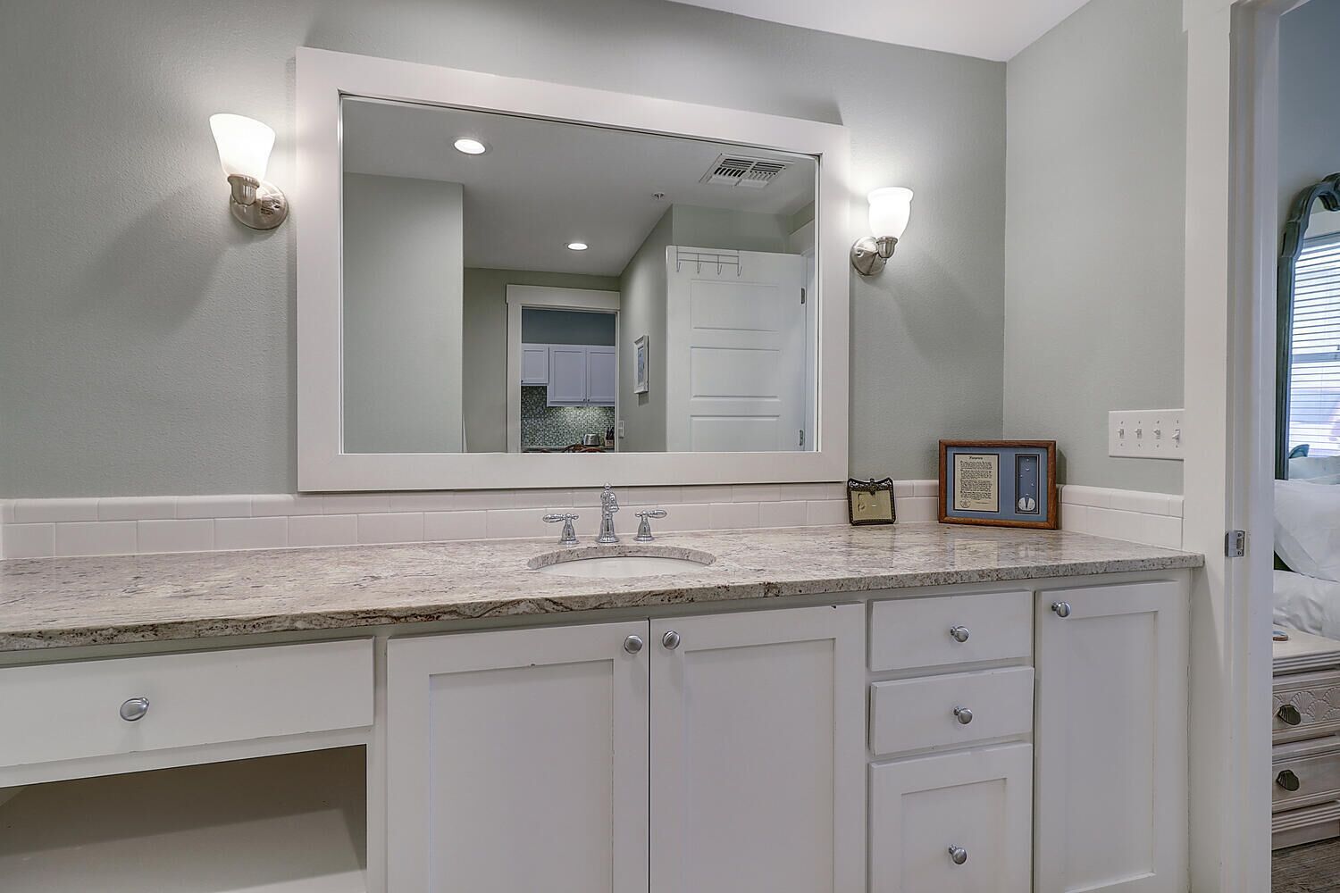 A bathroom with a large mirror, white cabinets, and a granite countertop.