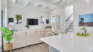 A modern living room with a beige sofa, a dining area with a white table, and a staircase leading to an upper level. - Isle of Dogs 205 Fiv-b (Port Aransas)