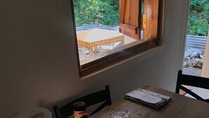 Ett matbord i trä med utsikt genom fönstret, en fjärrkontroll, ett glas och en kopp på ett litet fat.