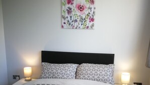 A neatly made bed with patterned bedding, two bedside lamps, and a floral artwork on the wall. - Bluewater House - Immaculate 4-bed in Greenhithe (Greenhithe)