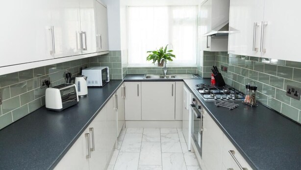 A modern kitchen with white cabinets, a black countertop, and a window with a plant. - Bluewater House - Immaculate 4-bed in Greenhithe (Greenhithe)