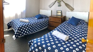Quarto com duas camas, cada uma com colcha azul estampada em branco, cômoda de madeira e um quadro na parede.