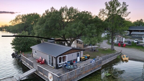 Uma cabana à beira do lago com um alpendre, área de estar externa e um cais para barcos.