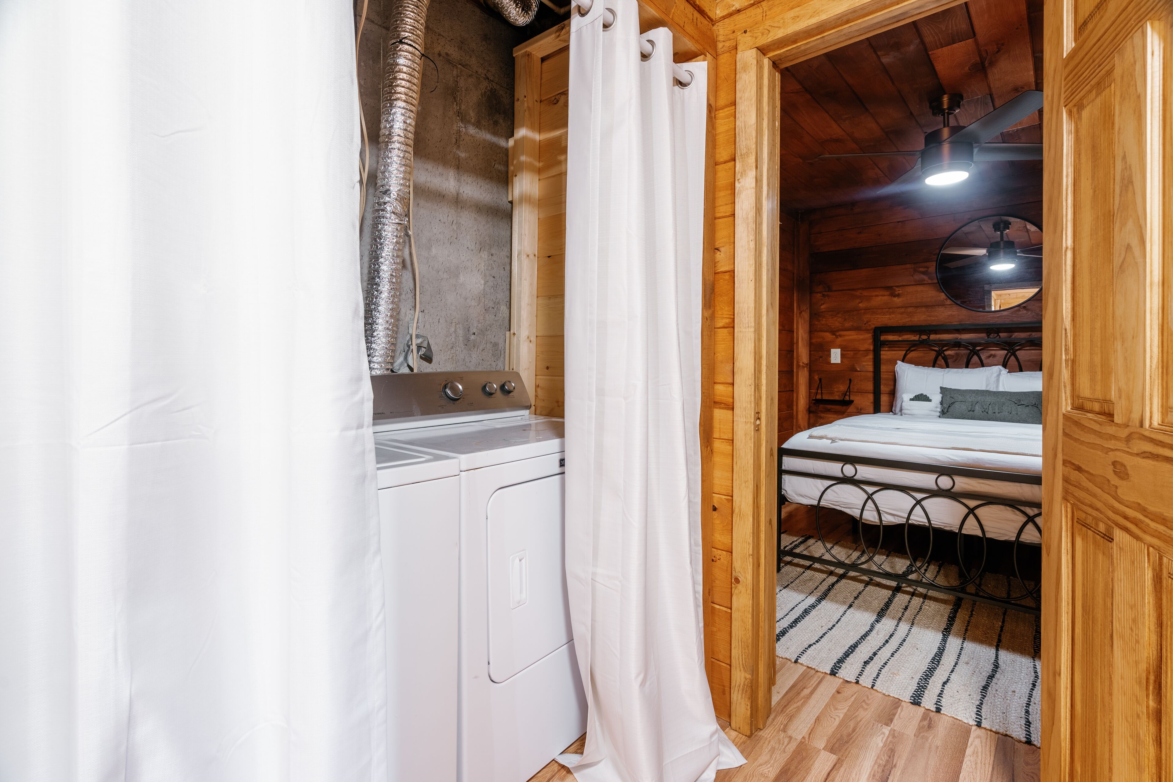 A wooden cabin bedroom with a bed, a washing machine, and a shower curtain.