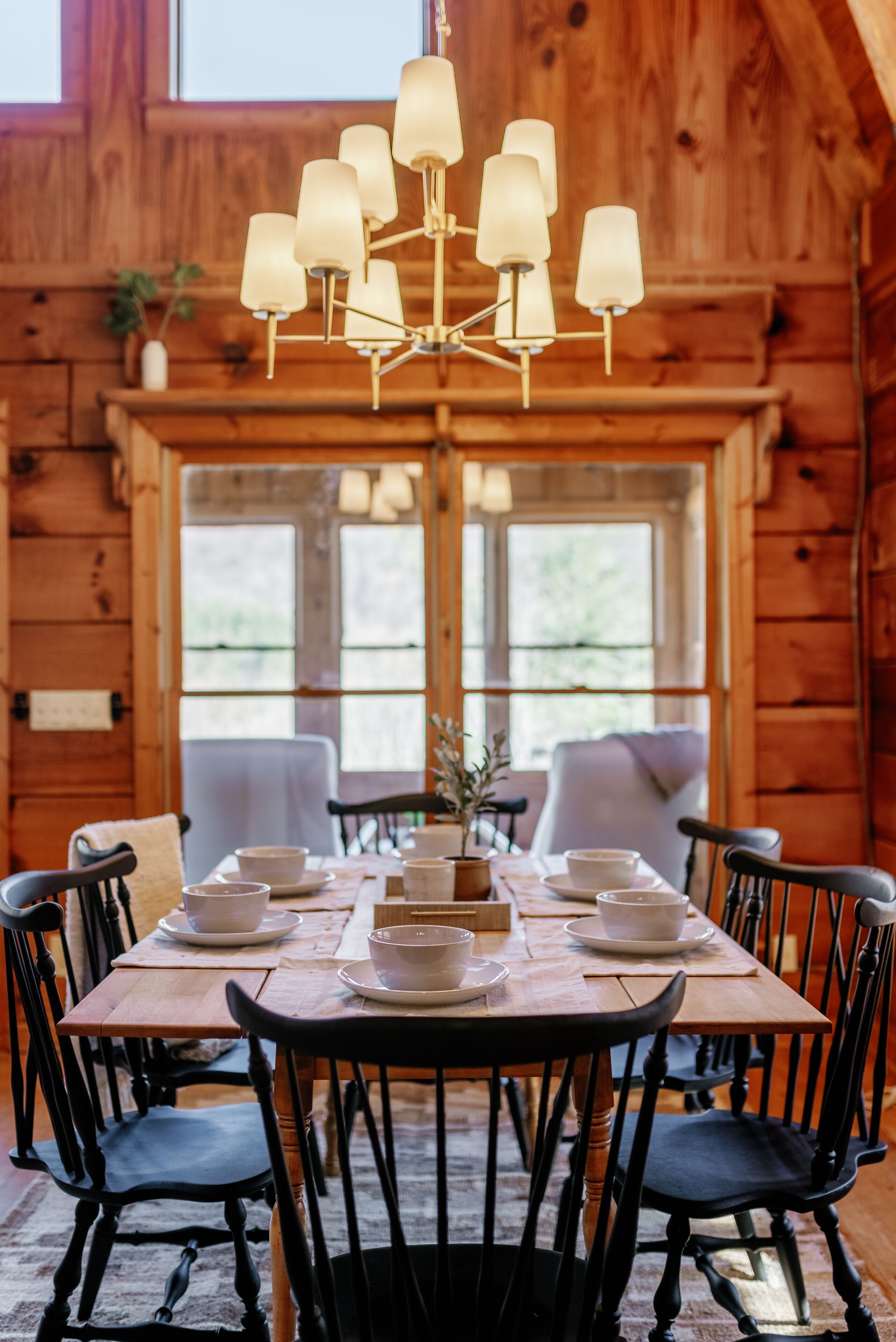 A wooden dining room with a chandelier, black chairs, and a table set for four.