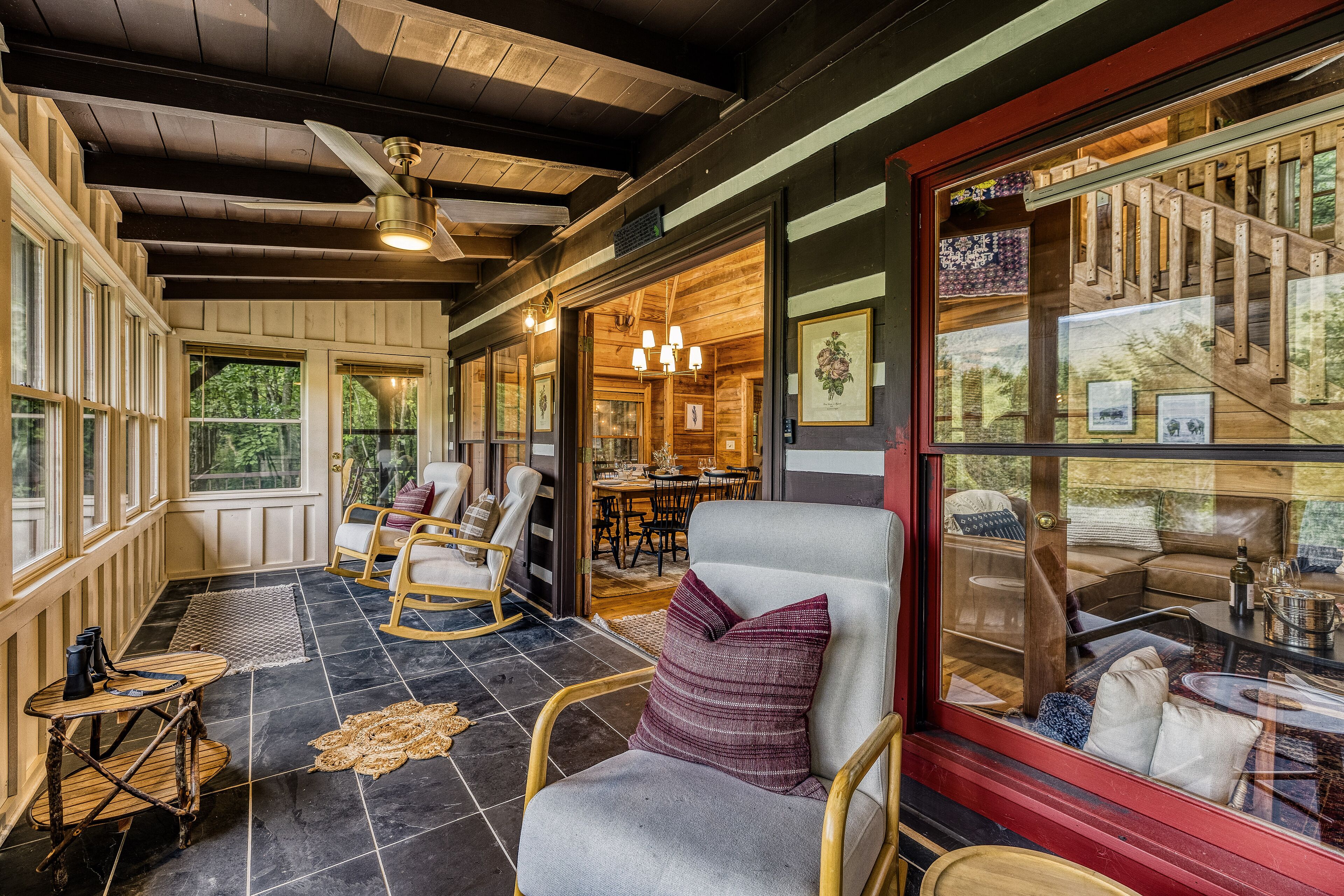 A cozy interior with wooden floors, rocking chairs, and a dining area visible through a glass door.