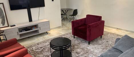 A living room with a TV, red and grey sofas, a small black table, and a red chair.
