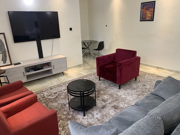 A living room with a TV, red and grey sofas, a small black table, and a red chair. - Beautiful Short-let Apartment in Lekki Phase 1 (Lekki)