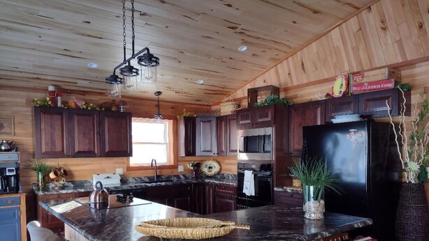 A kitchen with wooden cabinets, a black refrigerator, a marble island, and bar stools. - New Spacious Northwoods Lakefront Getaway (Phelps)