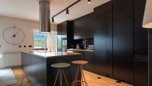 Une cuisine moderne avec des meubles de couleur sombre, un îlot central doté de tabourets et une grande fenêtre offrant une vue sur l’extérieur.