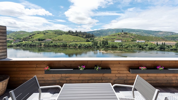 Une terrasse dotée de bancs en bois et de jardinières, offrant une vue sur un lac et des collines verdoyantes.