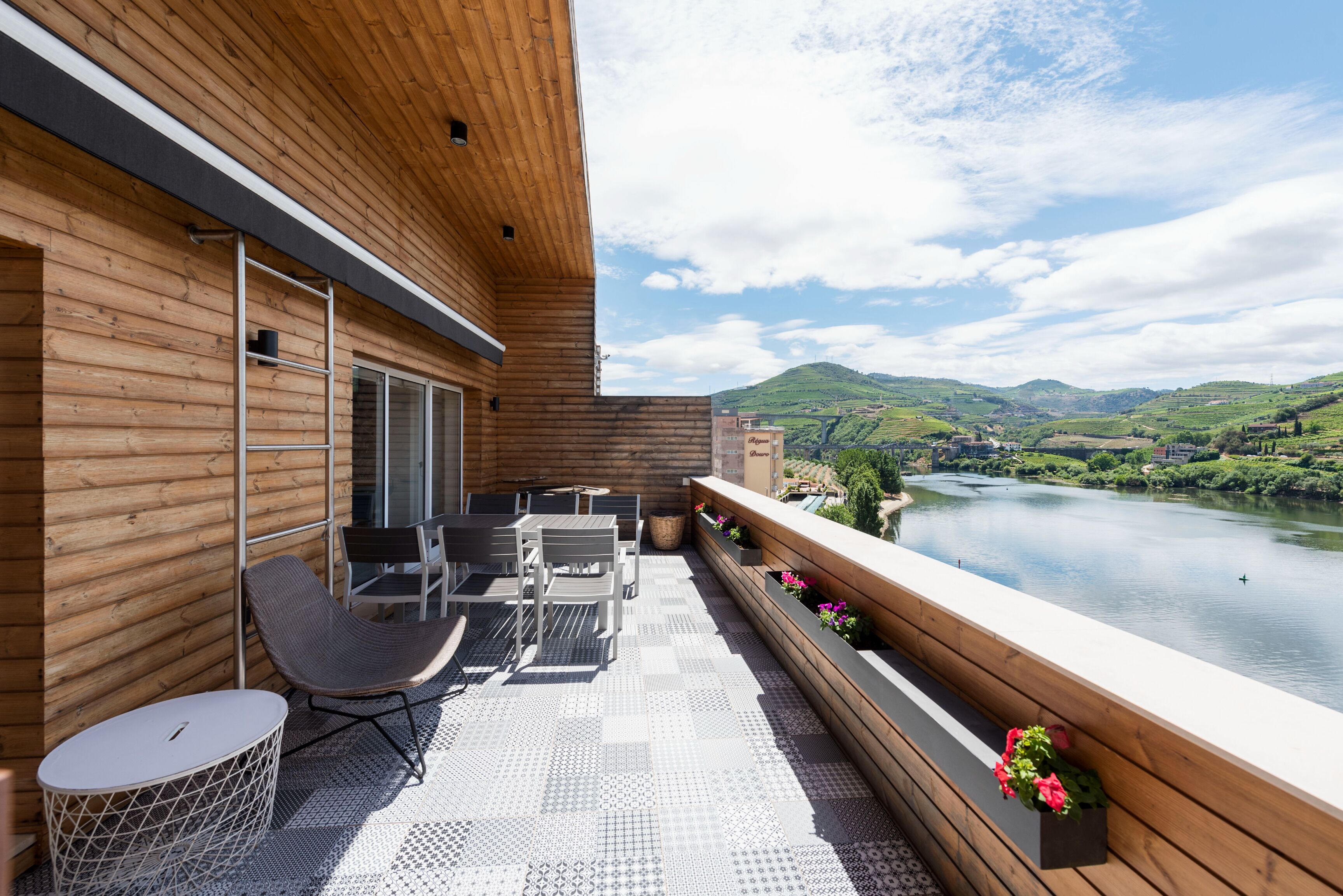 A wooden deck with outdoor furniture, overlooking a river and hills.