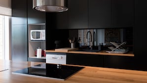Une cuisine moderne avec des meubles de couleur noire, une hotte de cuisinière en acier inoxydable, un four à micro-ondes et un plan de travail en bois.