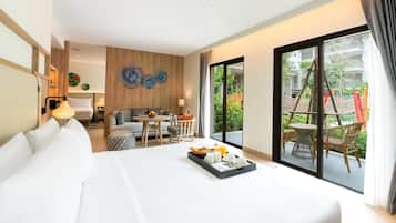 Habitación de hotel con cama, zona de estar con mesa y sillas, ventana grande con vistas a la vegetación y una pared de acento de madera.