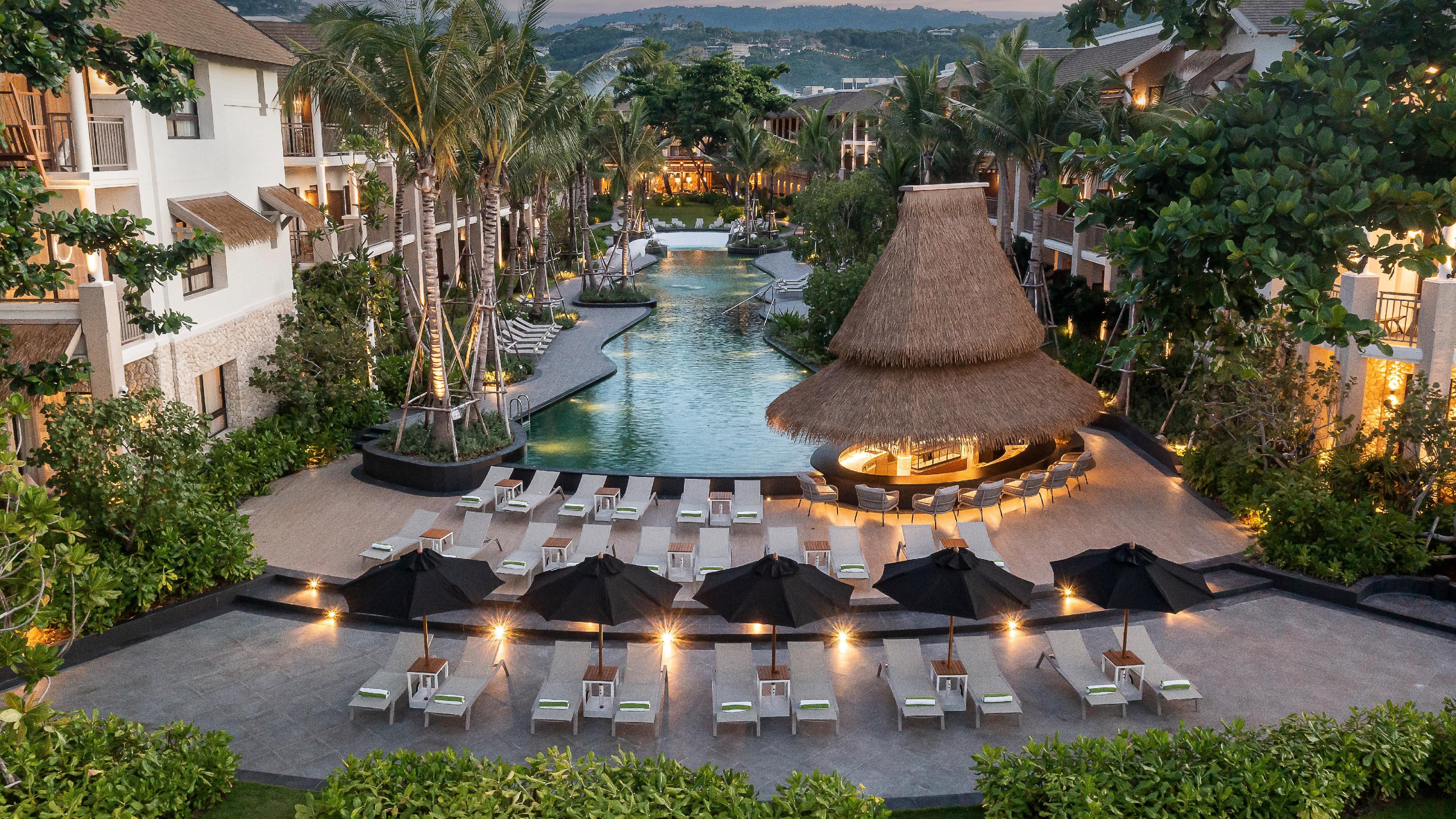 A resort with a central pool, lounge chairs, and a thatched-roof structure.