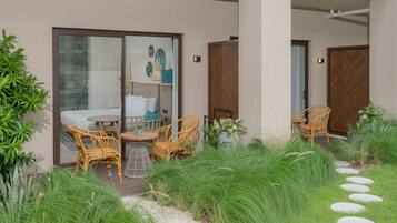 Un espacio al aire libre moderno con mobiliario de mimbre, una entrada con puerta de cristal y un jardín bien cuidado con piedras para caminar.