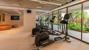 A modern gym with cardio equipment, a large TV, and a view of greenery outside.