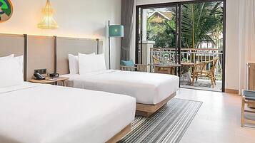 Habitación de hotel con dos camas, un escritorio, televisión y balcón con mobiliario exterior.