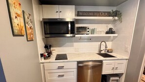 Una cucina compatta con mobili bianchi, lavastoviglie in acciaio inossidabile, microonde e forno tostapane. Si notano elementi decorativi appesi alle pareti e un cartello di benvenuto sopra il bancone.
