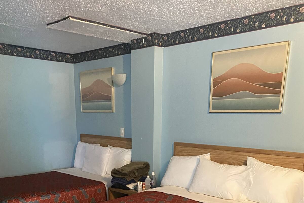 A hotel room with two beds, a wooden headboard, a nightstand, and two paintings on the walls.