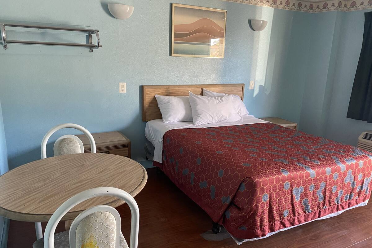 A bedroom with a bed, bedside table, chair, and a wall-mounted shelf.