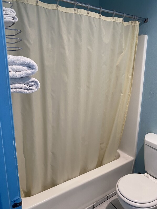 A bathroom with a beige shower curtain, a white bathtub, and a white toilet.